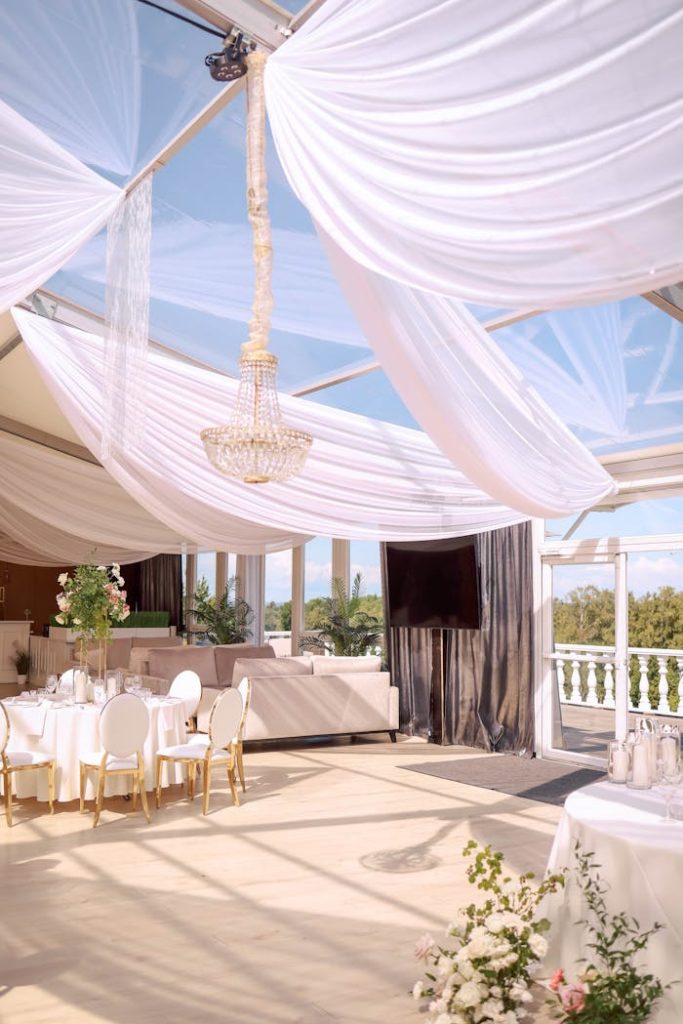 Spacious wedding venue with elegant drapery, sophisticated decor, and floral arrangements.